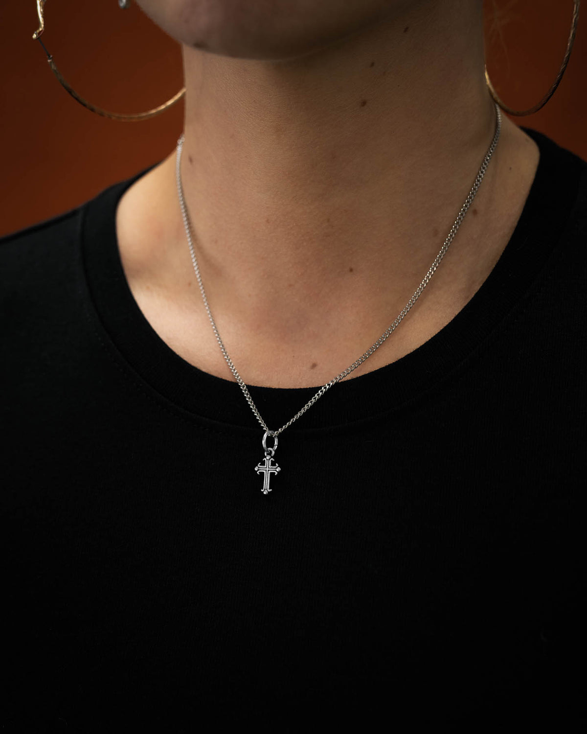 mini french cross pendant in 316L stainless steel on female model's neck against orange backdrop