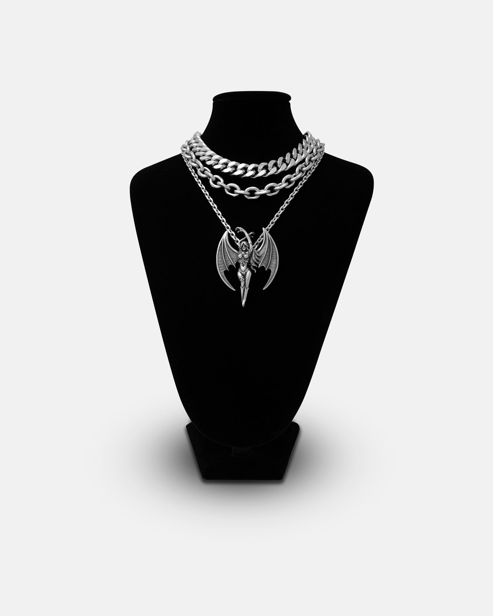 The Mistress Stack necklace, featuring a large winged demon pendant on a silver chain, is displayed on a black velvet bust and set against a white background—ideal for adding an edgy touch to your stack.