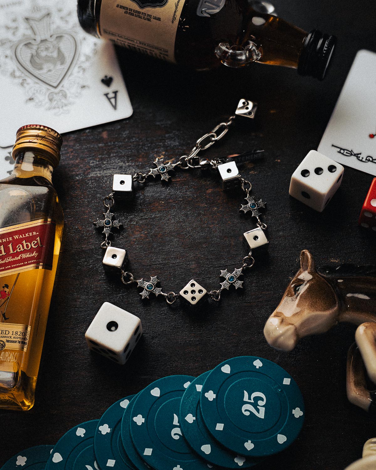 Bracelet with dice charms on a table with whiskey bottles, cards, and poker chips.