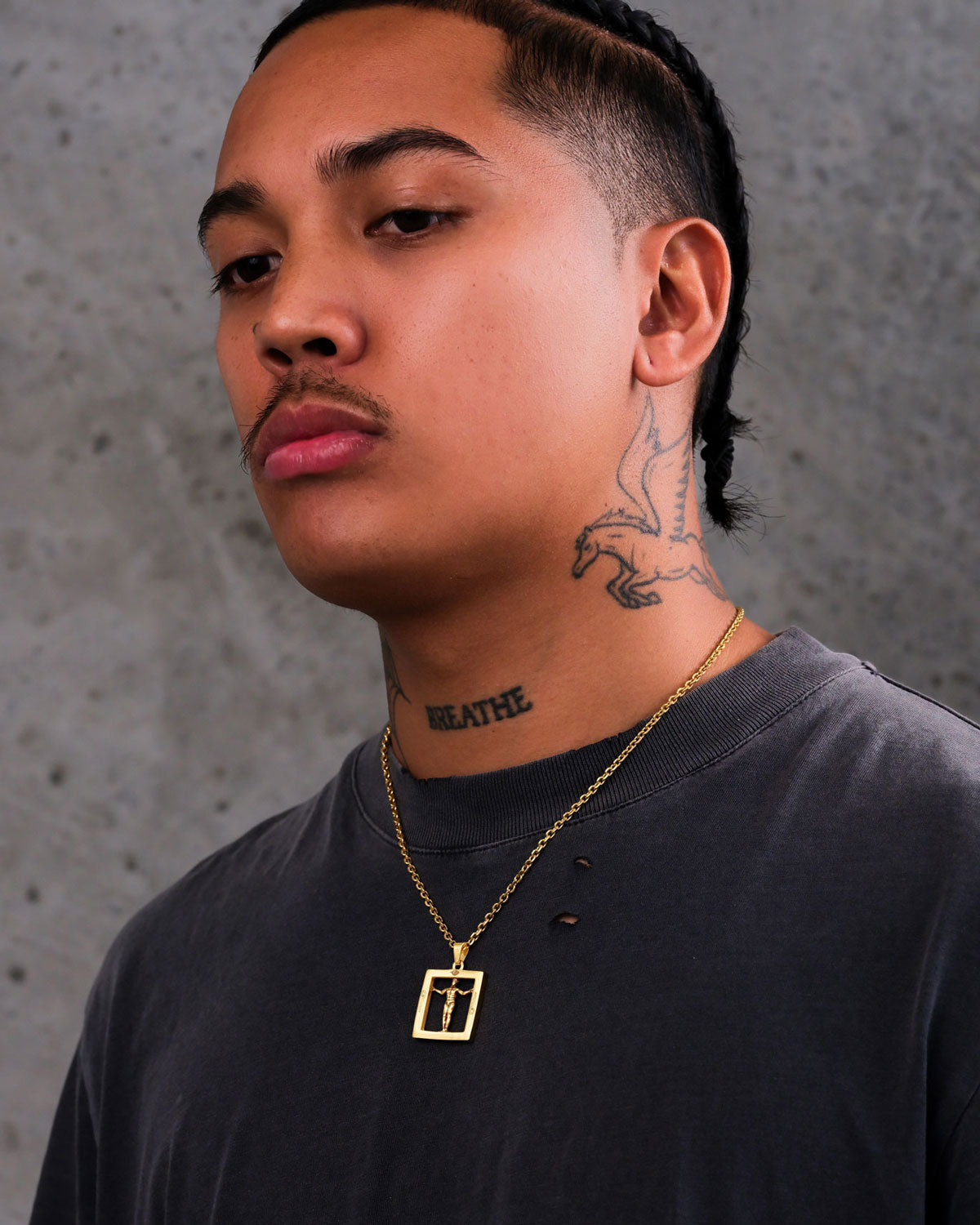 A person with a mustache and braids wears a gray t-shirt, gold necklaces featuring the Agrippa’s Square Pendant (Gold), and has neck tattoos—a dragon and the word BREATHE—against a textured gray wall.