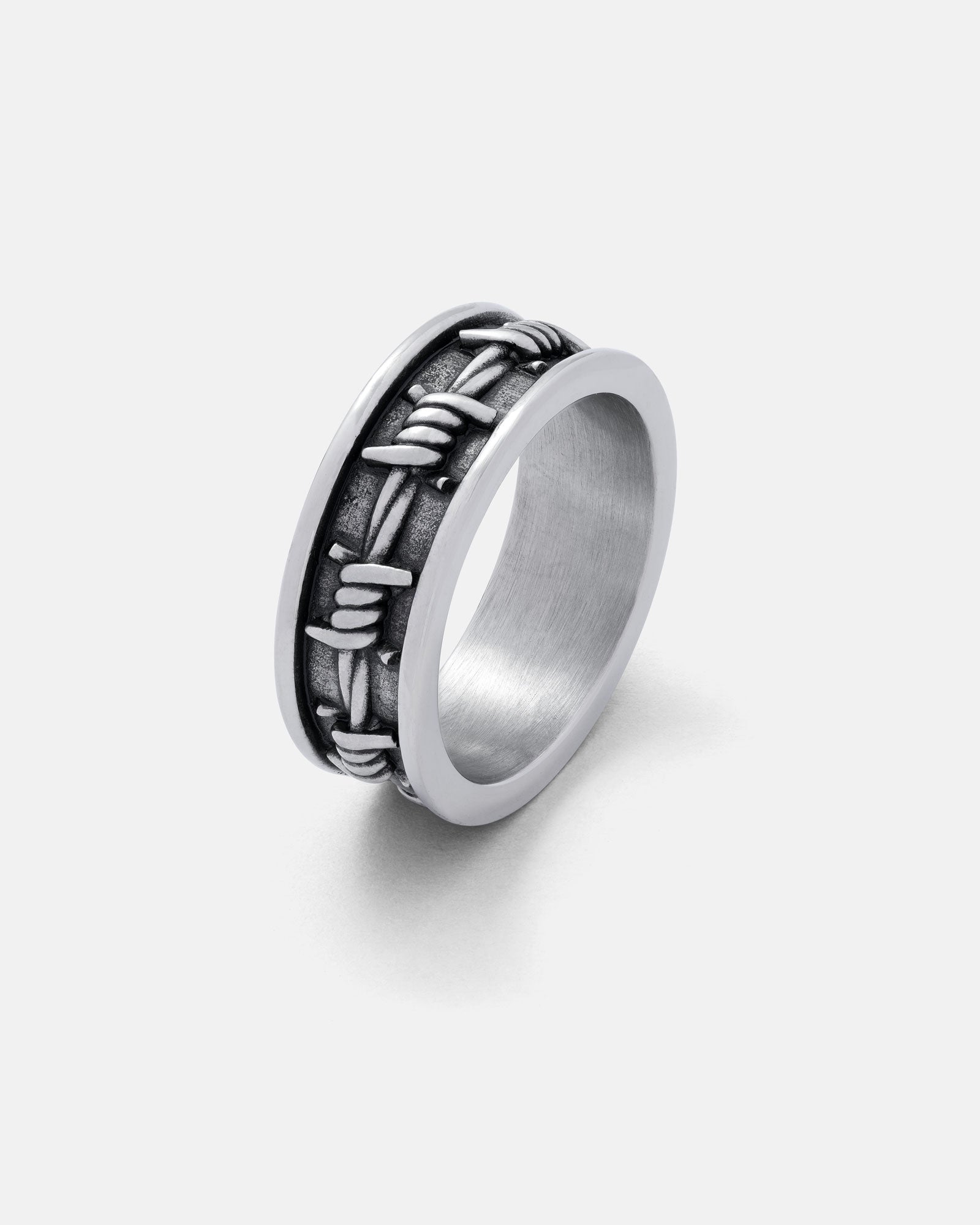 The Barbed Wire Ring features a silver, blackened band with a raised barbed wire design around the center. Set against a plain white background, it's perfect for stacking and adds an edgy touch to any look.