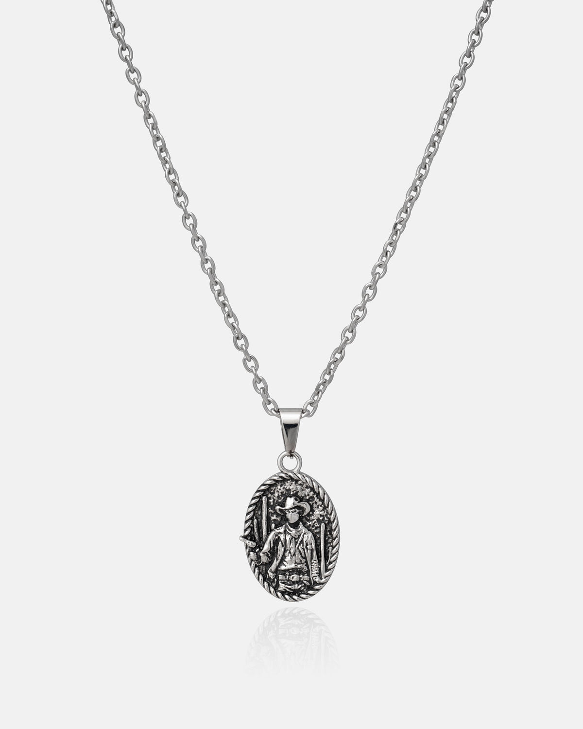 The "Big Iron" Pendant by STATEMENT is a silver chain necklace featuring an oval-shaped stainless steel pendant with a detailed engraving of a religious figure, possibly a saint, surrounded by intricate decorative elements. Combining elegance and durability, this pendant stands out against a plain white background.