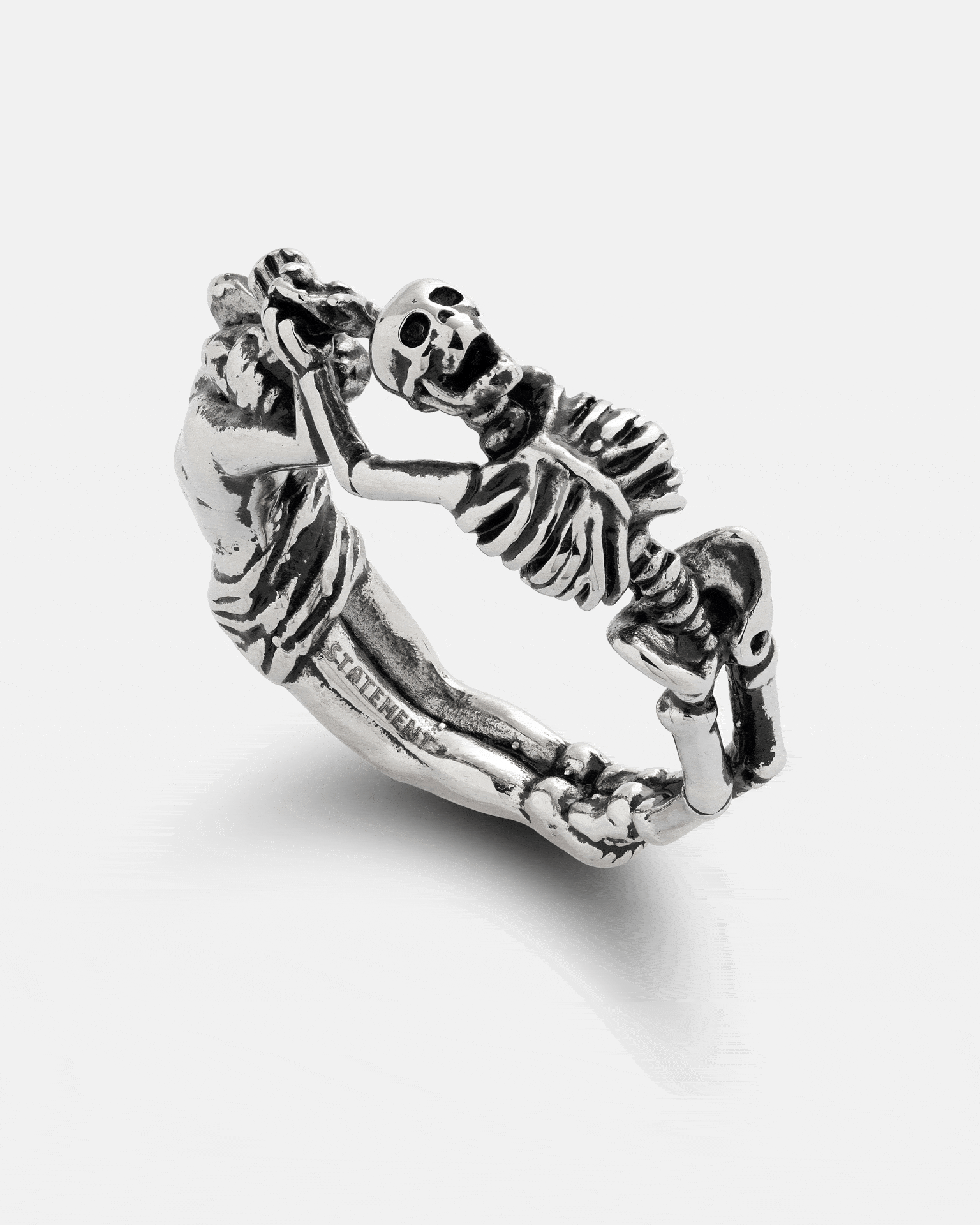 Statement Collective Breaking Wheel ring in silver, featuring a sculpted figure and a skeleton facing each other.