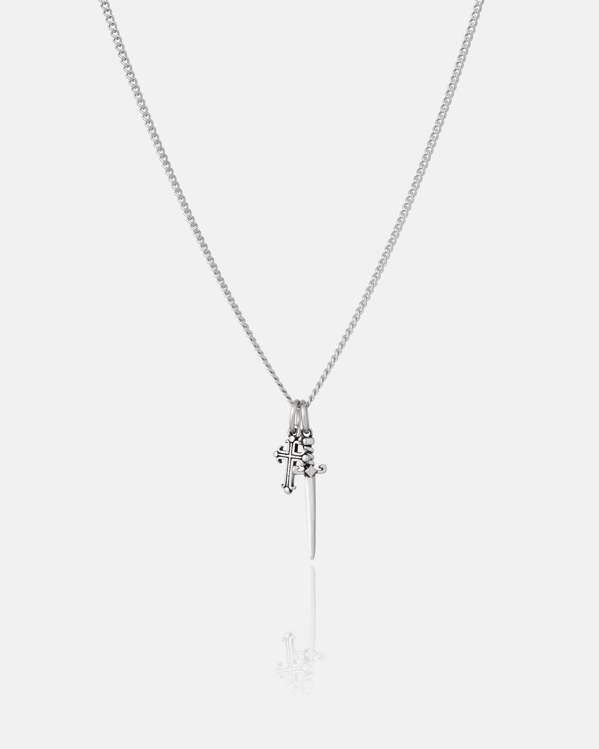 The Cross & Dagger Necklace by Statement Collective features two striking stainless steel pendants—a detailed cross and a sleek, minimalist dagger—suspended gracefully from a fine chain. This evocative piece channels a dark romantic aesthetic, beautifully showcased against a plain white backdrop.