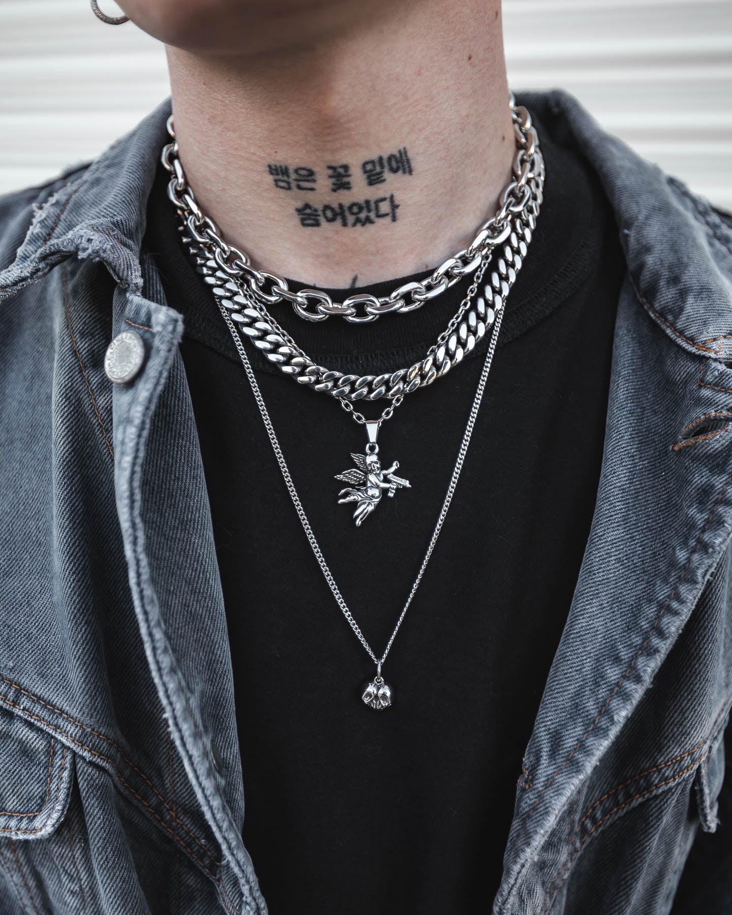 Wearing the Dead Love Stack, a grunge necklace set featuring layered silver chains and a skull heart pendant, over a black shirt and denim jacket; a tattoo with Korean text is visible on their neck.