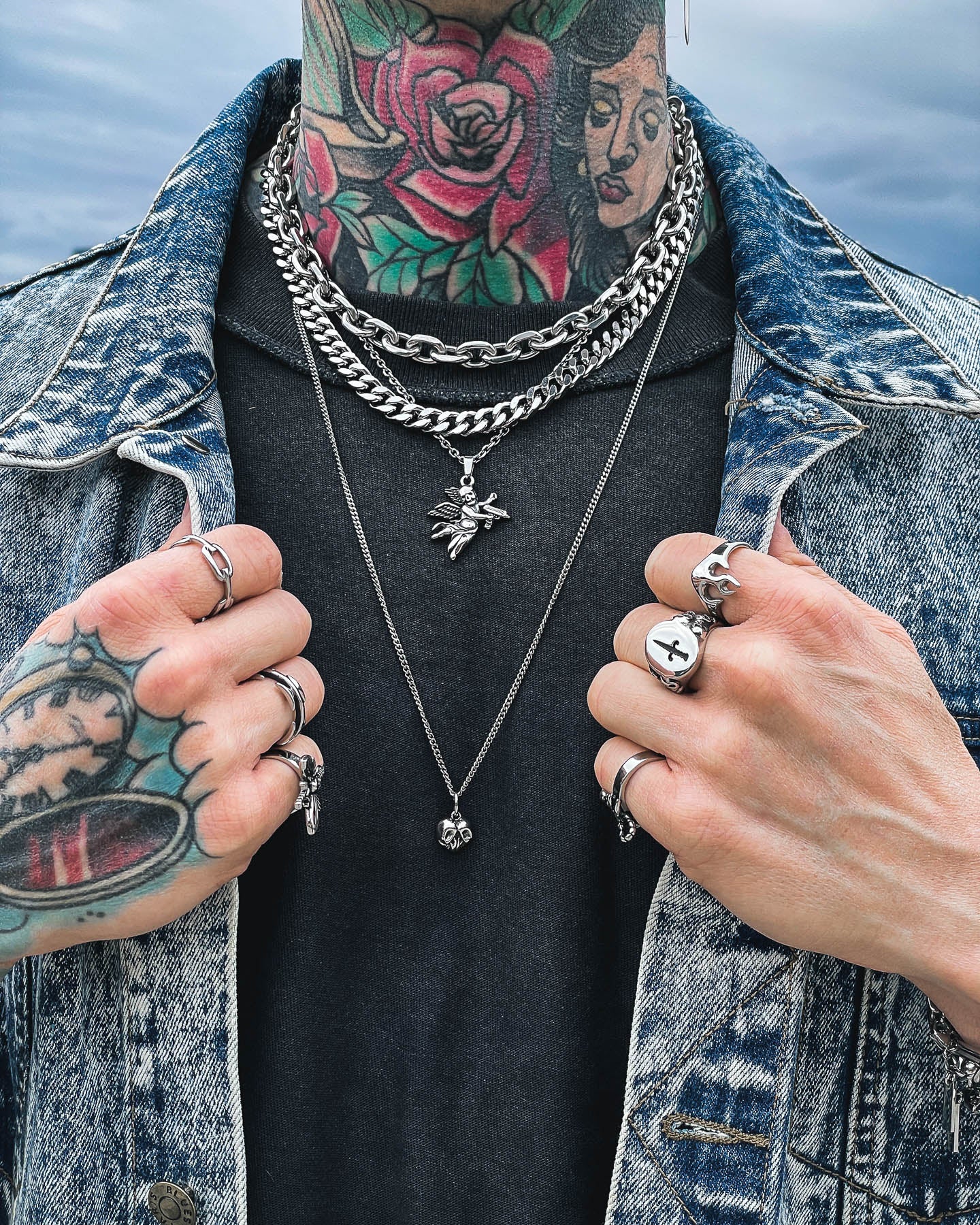 Wearing the Dead Love Stack layered over a black shirt and blue denim jacket, a person with vibrant rose and woman's face tattoos and multiple rings completes their edgy, distinctive look.