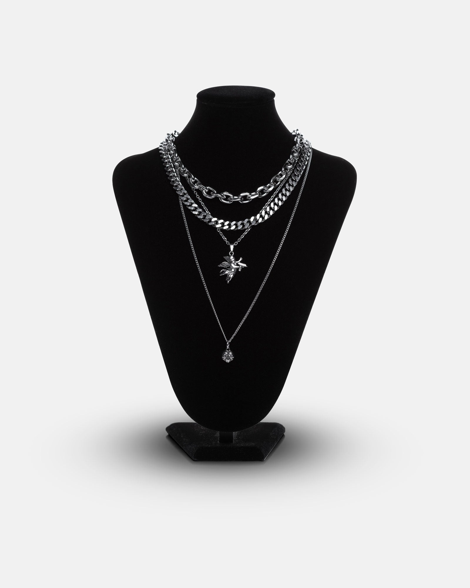 A black jewelry bust showcases the Dead Love Stack, a grunge necklace set with four silver necklaces of varying lengths and styles—chunky chains and layered pendants including a leaf and round charm—against a plain white background.