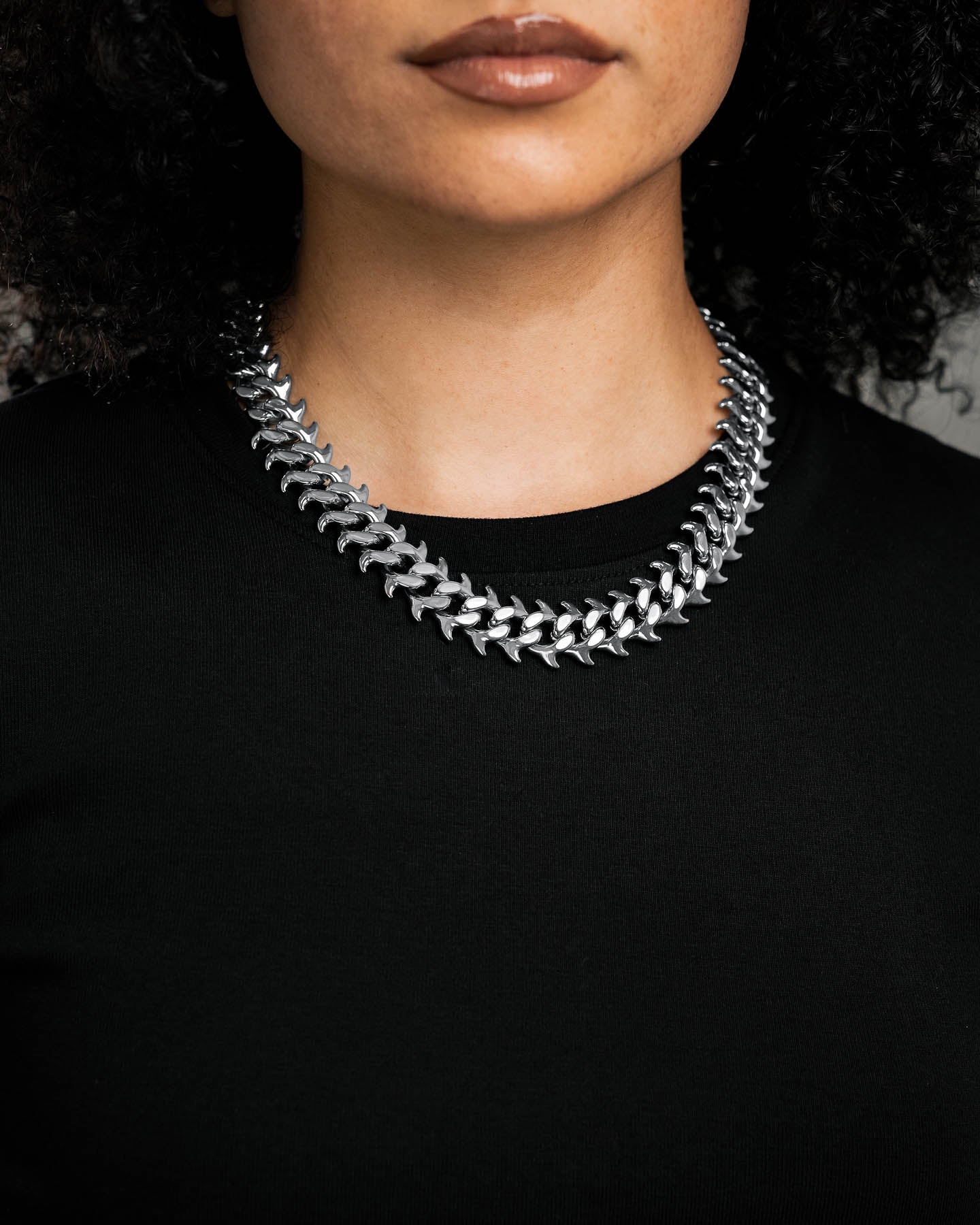 A person in a black top wears the "Fishbone" Curved Spike Cuban Chain, shown shoulders up against a neutral background with focus on the chain's custom links.