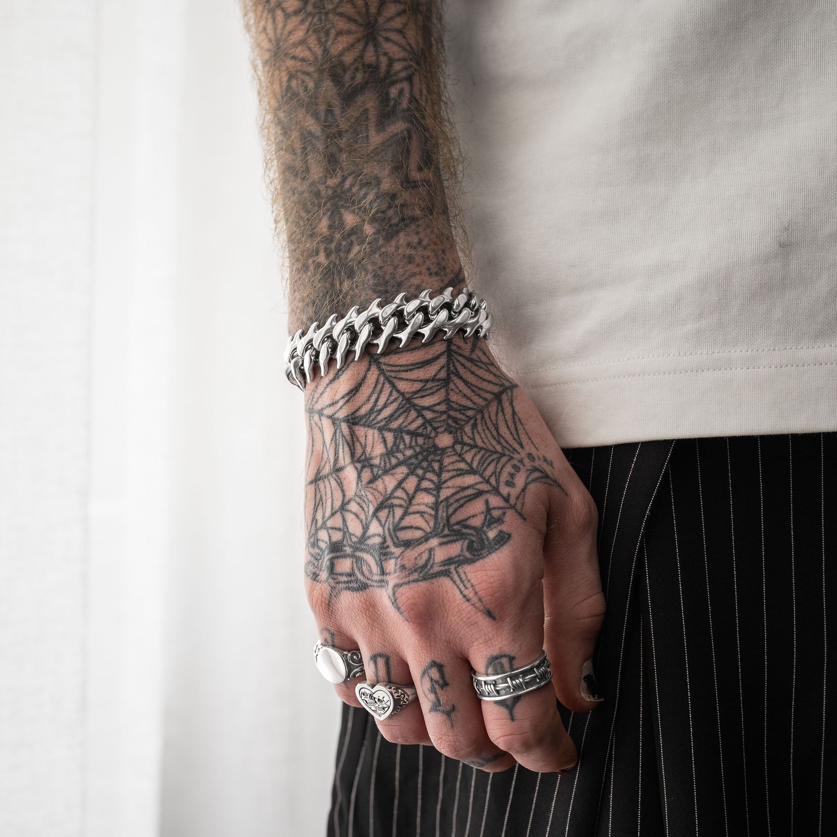 Tattooed men's hand wearing fishbone style spiked cuban bracelet by statement collective