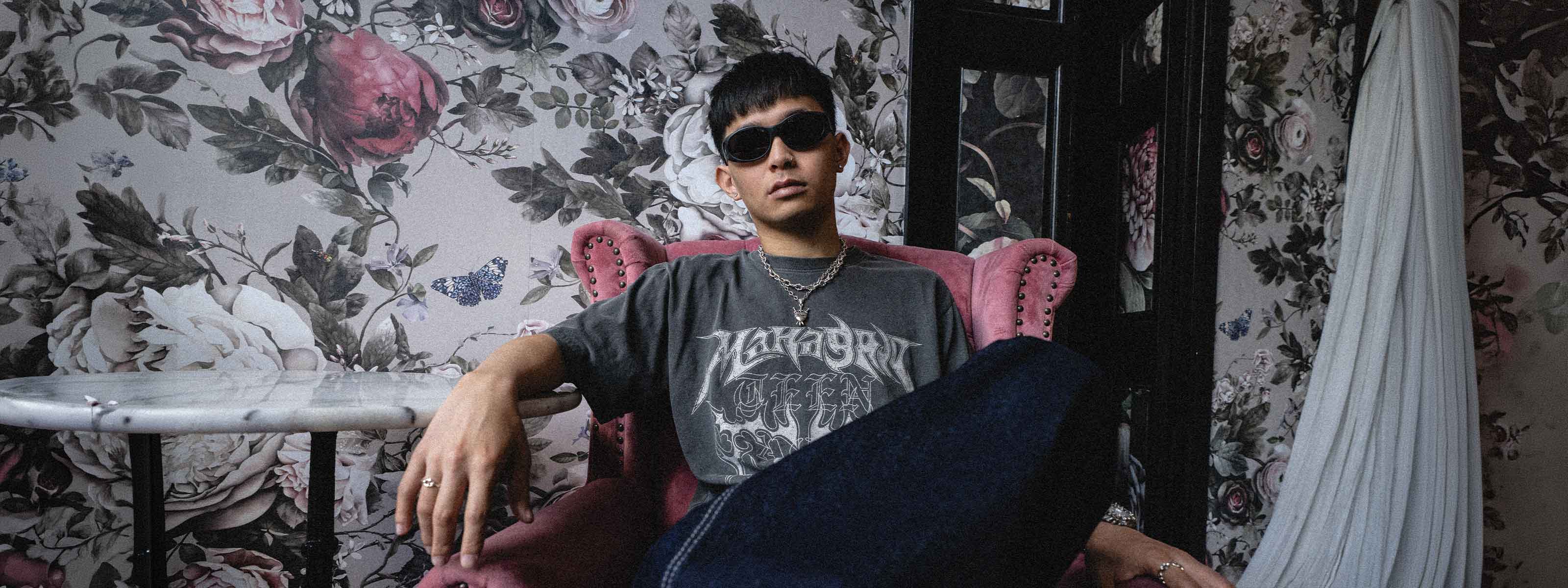 male model sitting on a pink velvet chair, wearing grey graphic tee, and the 925 sterling silver 9mm spiked cathedral necklace as well as the 3 of swords pendant on the 6mm spiked cathedral necklace