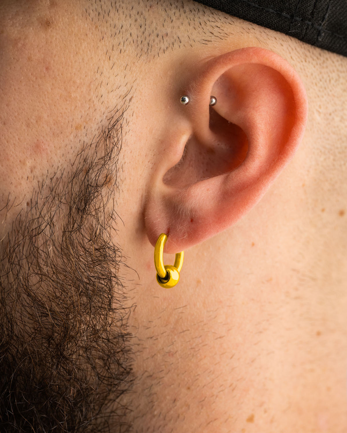 A hypoallergenic 18k gold-plated Statement Collective Ball Hoop Earrings (Gold) featuring a single sliding bead, worn in an earlobe.