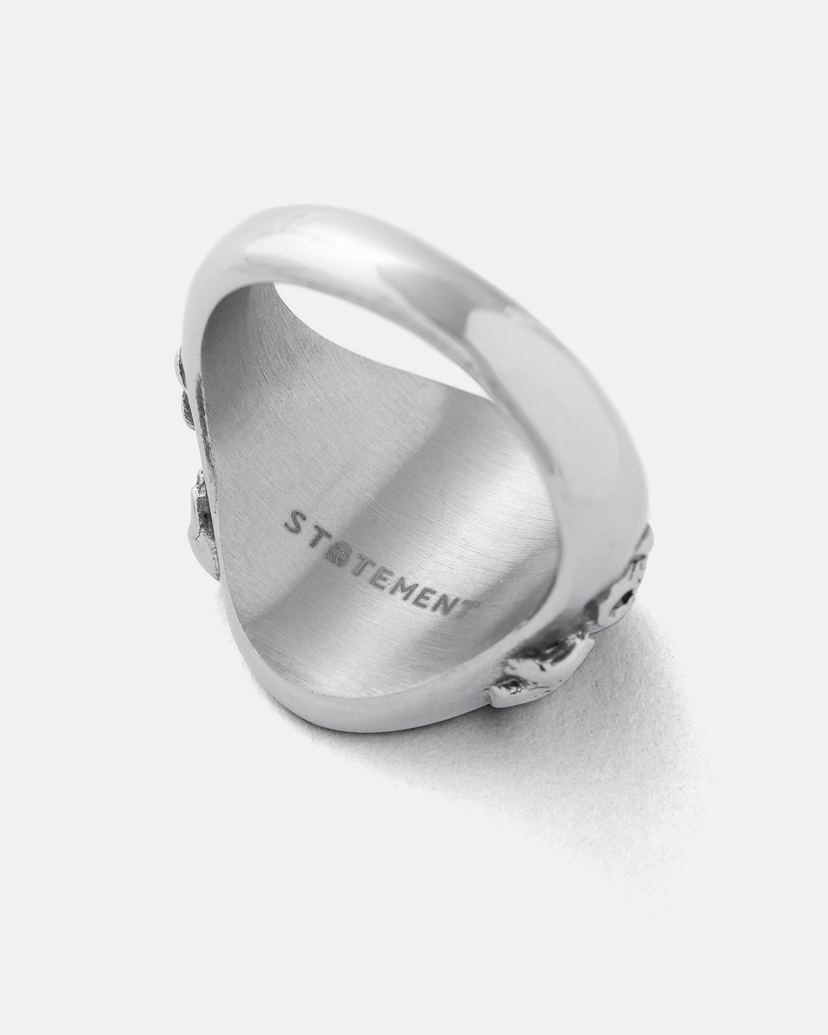 A silver stainless steel Graveyard Signet Ring by Statement Collective, displayed at an angle to emphasize the inner STATEMENT engraving and its polished, gleaming surface—a subtle tribute to the ring’s bold character.
