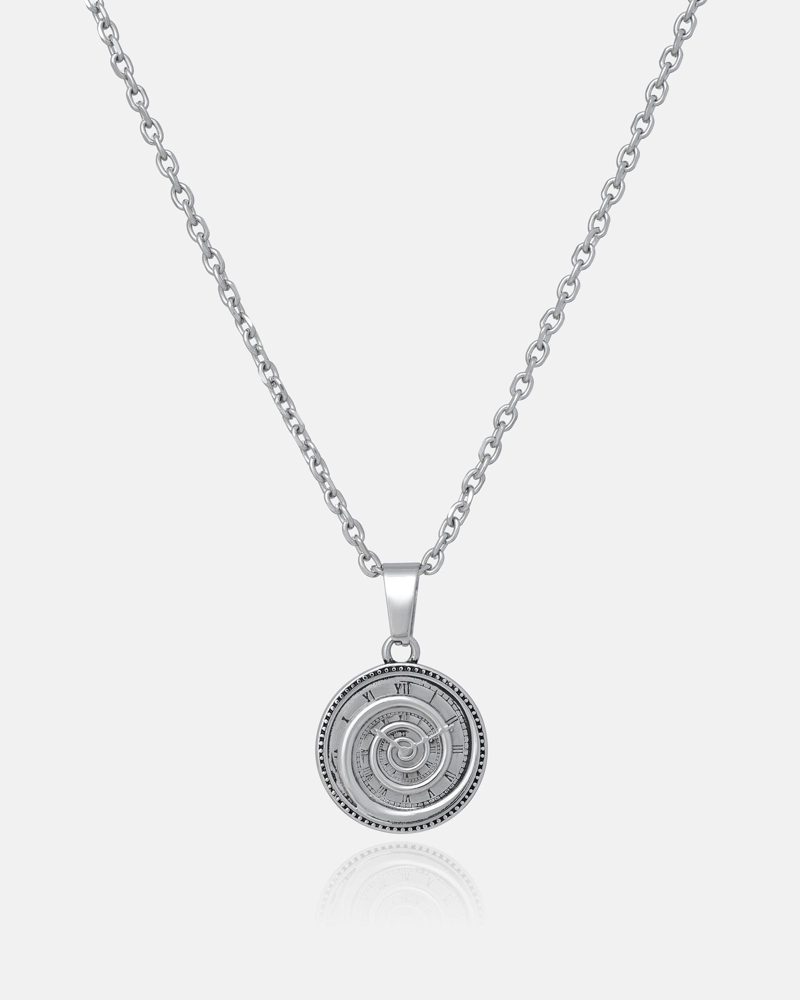 The Infinite Clock Pendant Necklace features a silver chain and a round clock pendant with an intricate spiral design and Roman numerals, showcased against a plain white background.