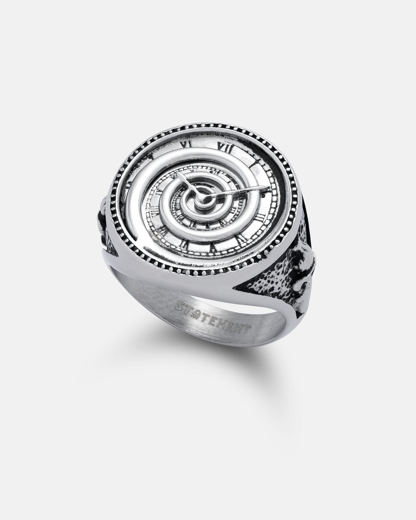The Infinite Clock Ring is a silver spiral ring with intricate jewelry design, Roman numerals, and geometric patterns on a white background. The inside band features an engraving of the word STATEMENT.
