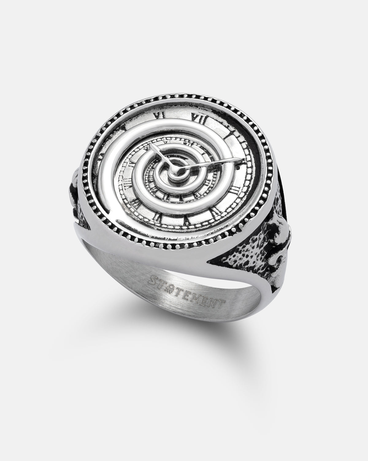 The Infinite Clock Ring by Statement Collective is a silver ring intricately designed to resemble a spiral clock face, complete with Roman numerals, clock hands, and textured edges. The inner band is inscribed with “STATEMENT.”.
