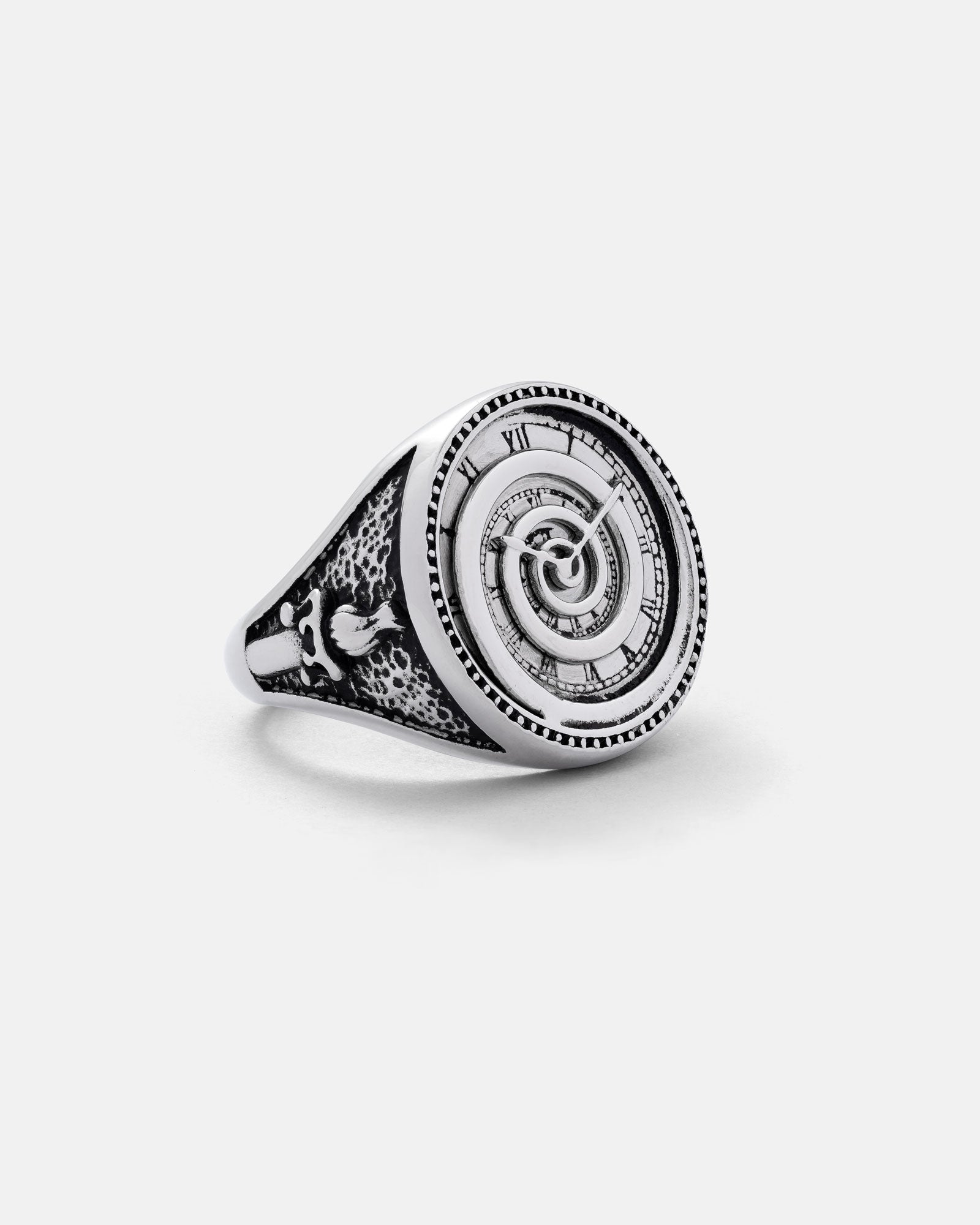 The Infinite Clock Ring by Statement Collective is a stainless steel piece featuring a round face with Roman numerals, a spiral clock design, an engraved patterned band with a bird motif, all set against a plain white background.