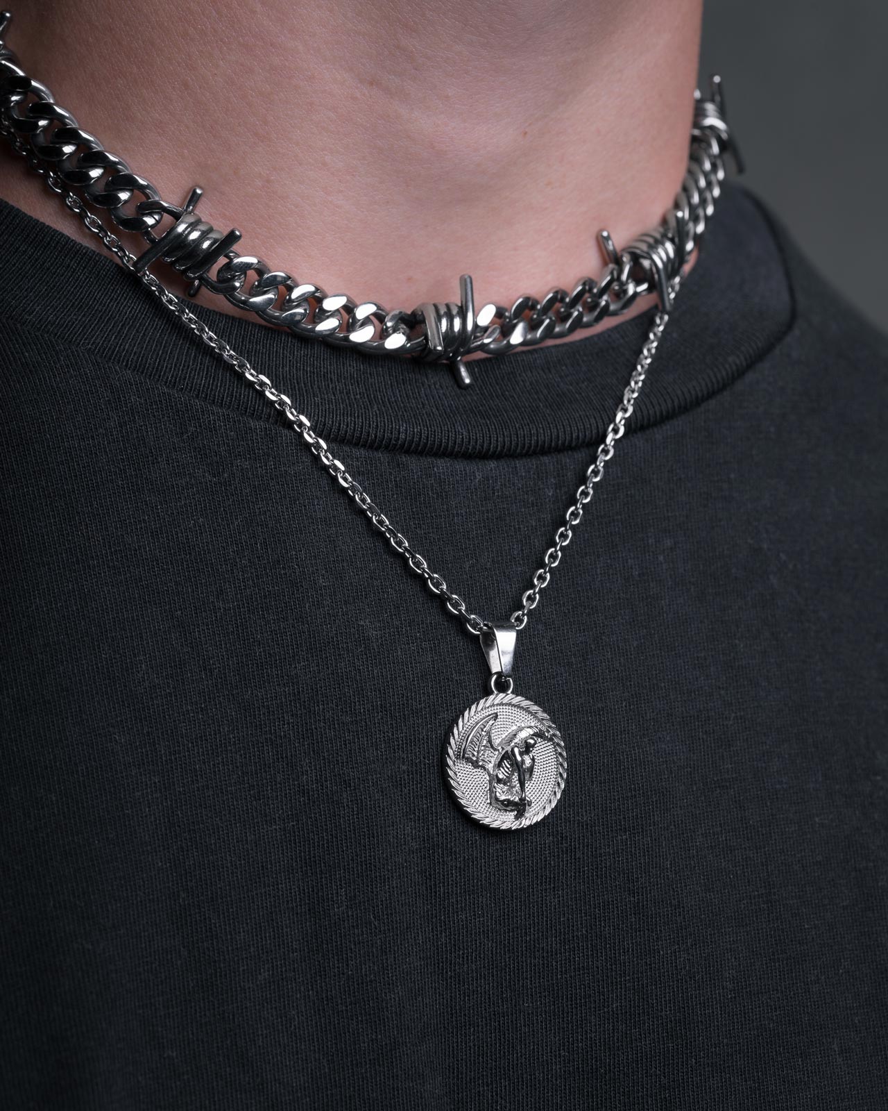 Wearing Statement Collective’s thick silver barbed wire choker and their Fallen Angel Medallion Pendant necklace, both stand out against a black shirt.