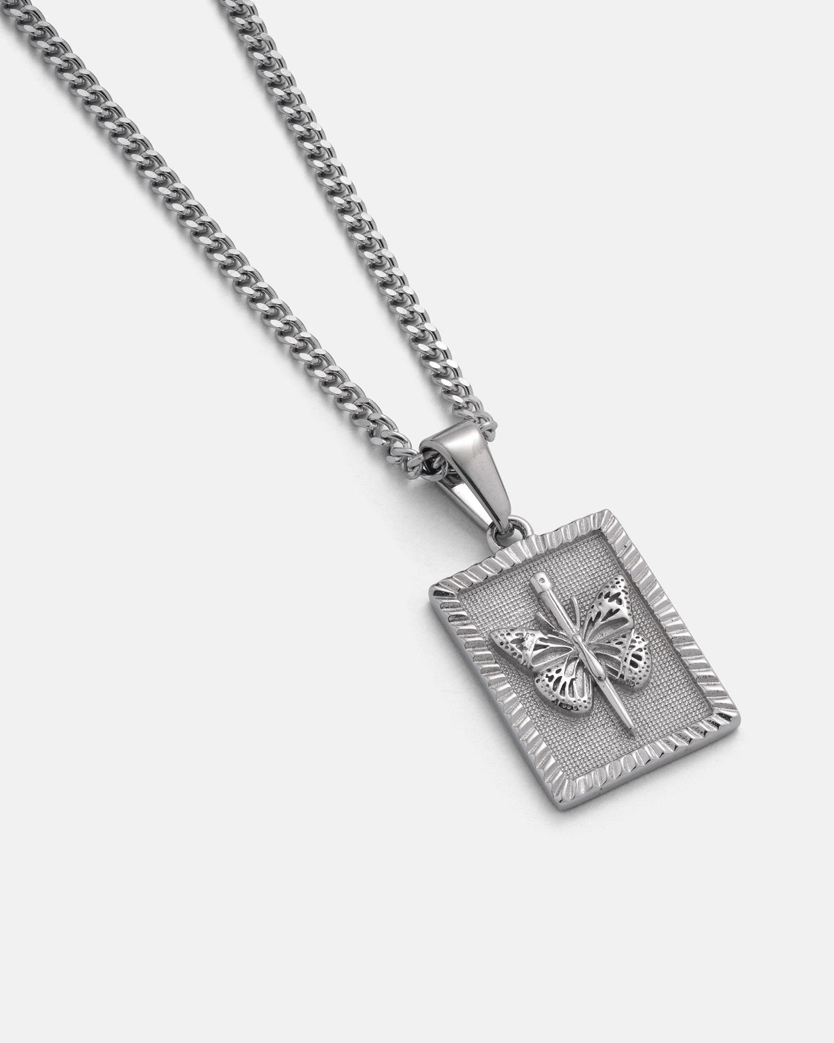 The Statement Collective Mini Butterfly Tag Pendant is a silver chain necklace featuring a rectangular stainless steel pendant embossed with an intricate butterfly design at its center, showcased on a plain white background.