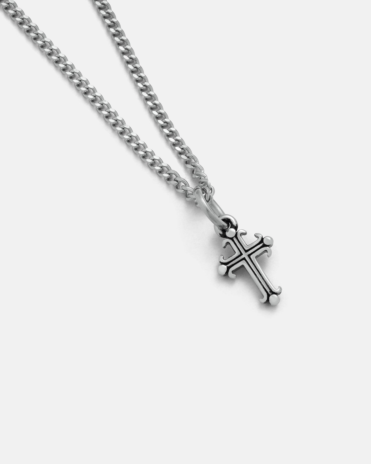 The Mini French Cross Pendant by Statement Collective, a silver chain necklace featuring a decorative cross that exemplifies dark romance jewelry, is displayed on a plain white background.