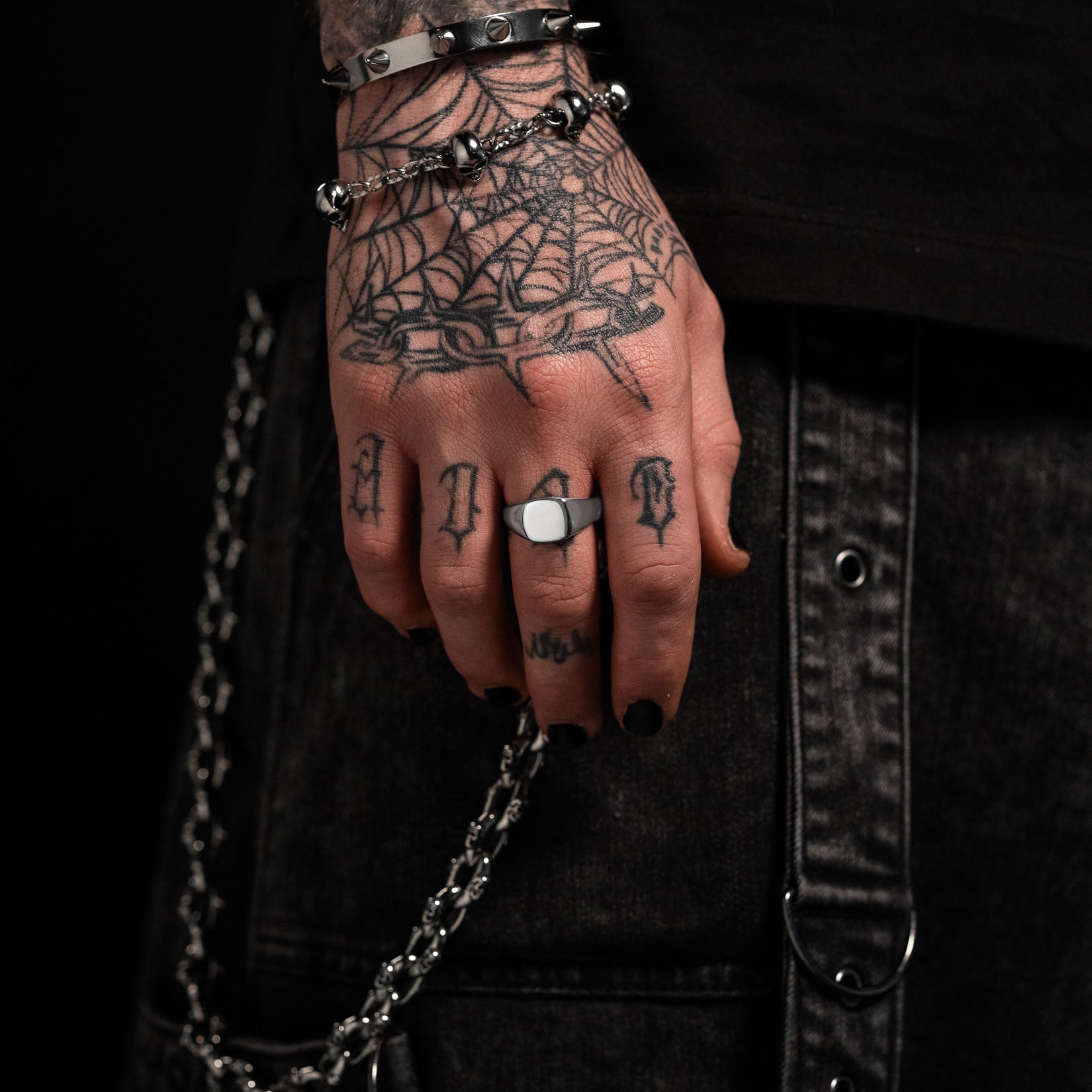 Hand with tattoos and jewelry against a dark background by statement collective