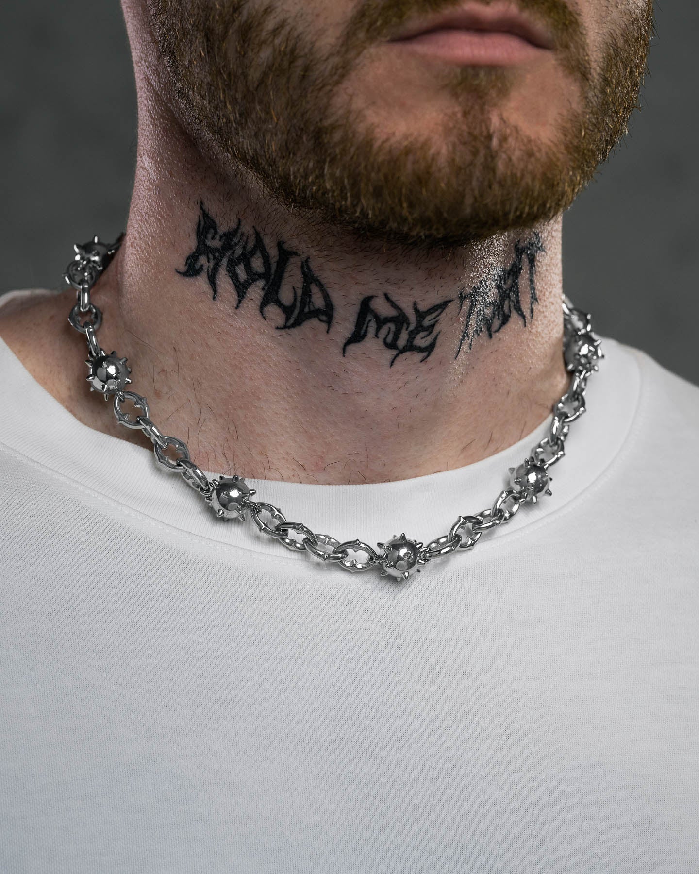 A bearded man in a white shirt wears a chunky "Morning Star" Cathedral Chain necklace. He has “HOLD MY ART” tattooed in bold, stylized black letters on his neck.