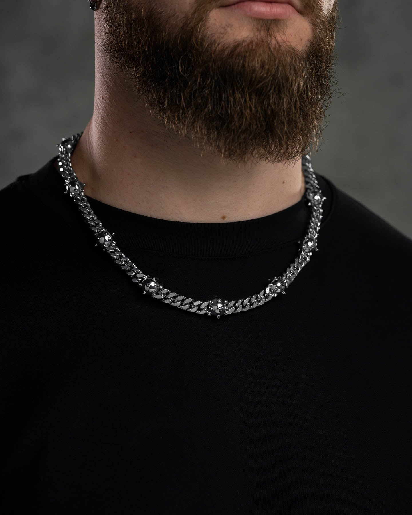 A person with a brown beard wears a black shirt and the "Morning Star" Cuban Chain, featuring small silver decorative elements. The background is dark and blurred.