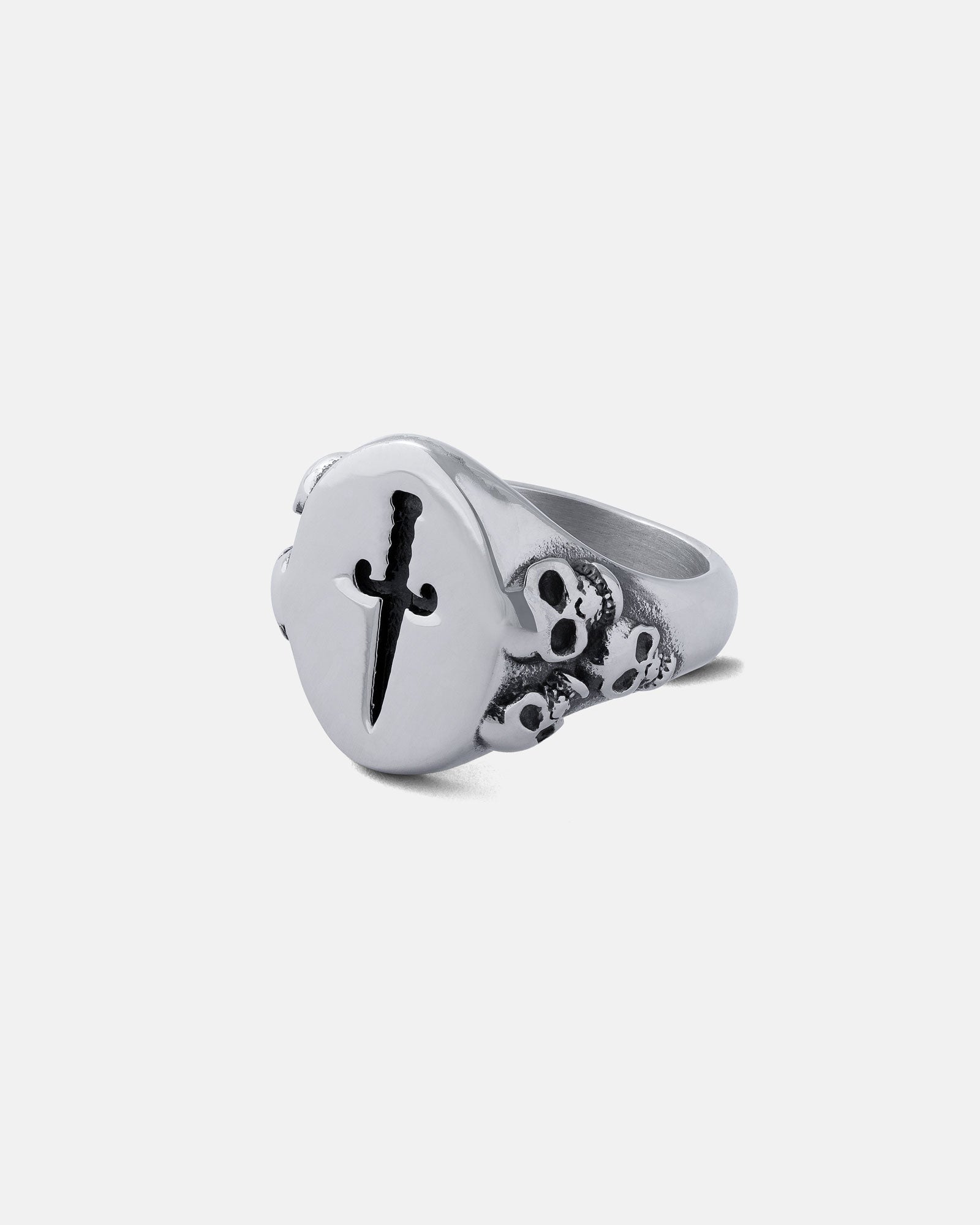 The Graveyard Signet Ring is a silver signet ring with a flat circular top engraved with a black dagger and three small skulls on the band, blending classic graveyard style with edgy design.