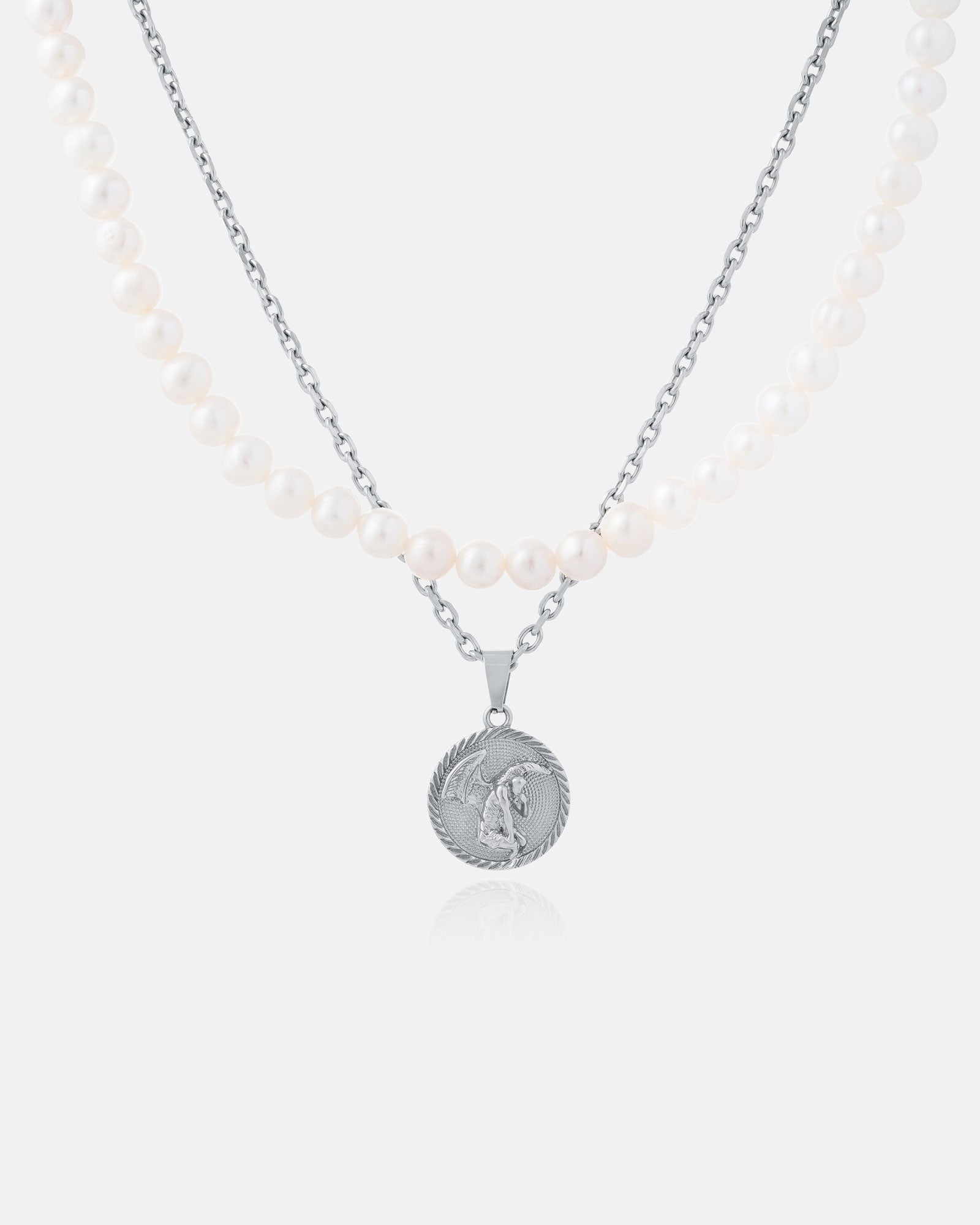 The Pearl Set (Custom Pendant Choice) features a freshwater pearl necklace with two strands—white pearls and a silver chain—and a round silver pendant engraved with a winged figure, shown on a plain white background.