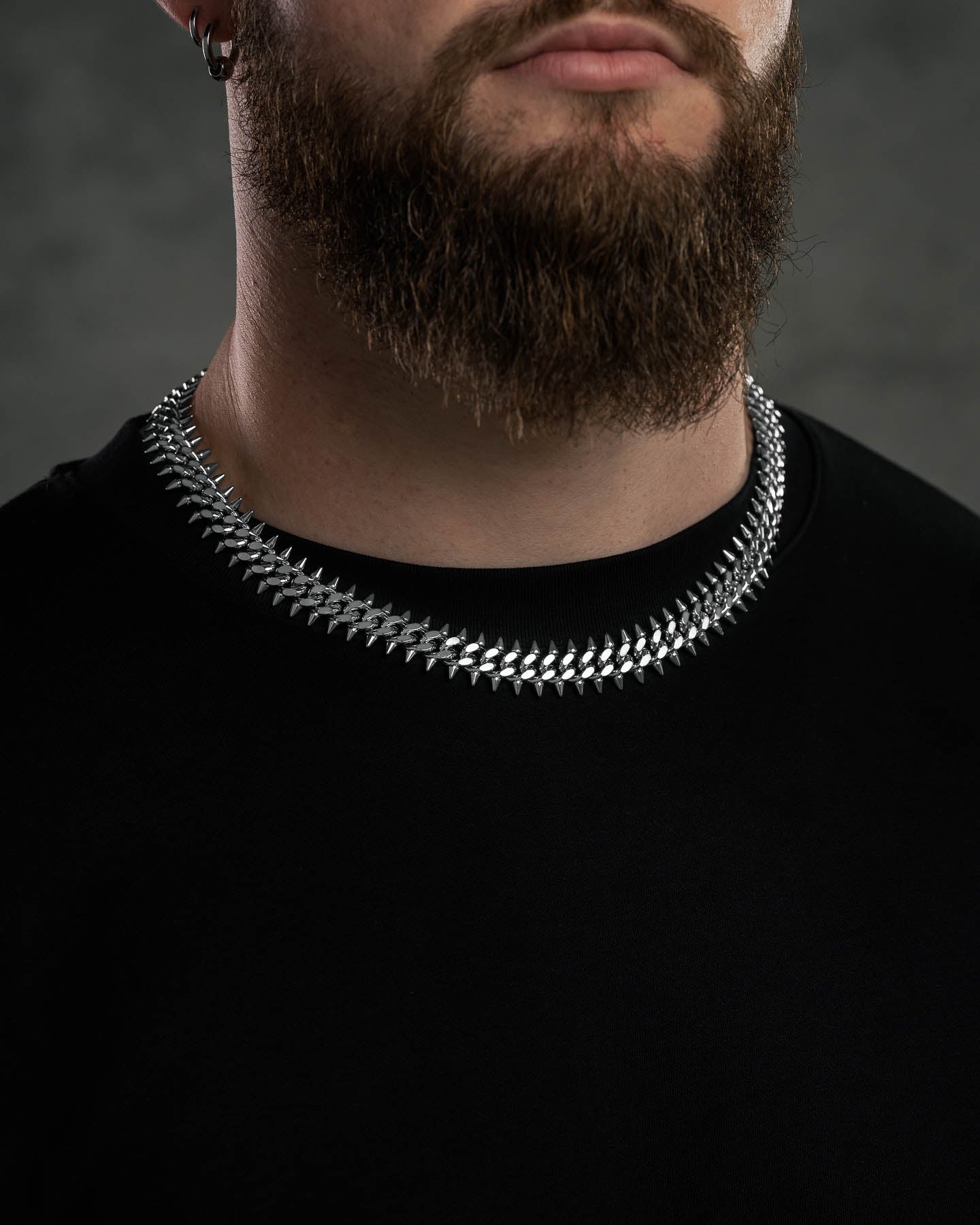 A man with a full beard and mustache wears a black shirt and the "Screwed Up" Spiked Cuban Chain crafted from 316L stainless steel. His face is partially visible, with focus on his neck and the shiny necklace against a dark background.