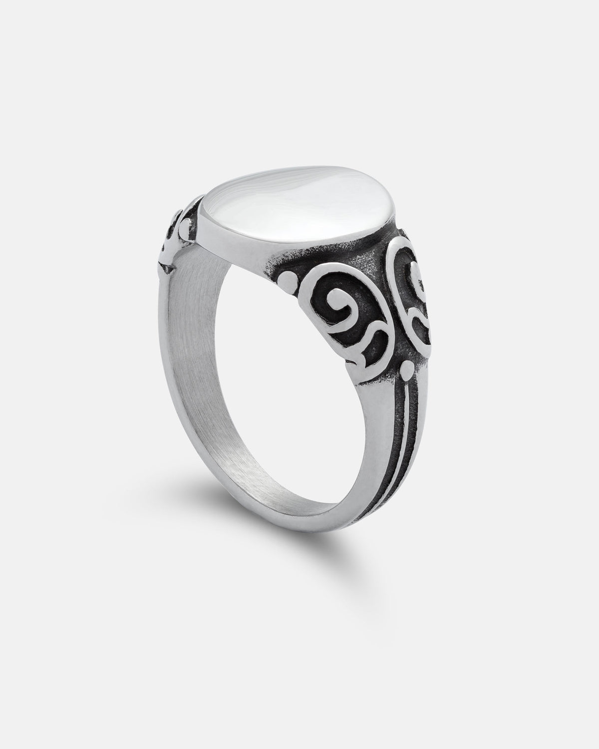 The Mini Oval Scroll Signet Ring by Statement Collective is a silver ring featuring a smooth white stone atop an oval setting, with black traditional scroll pattern designs adorning the band, displayed against a plain white background.