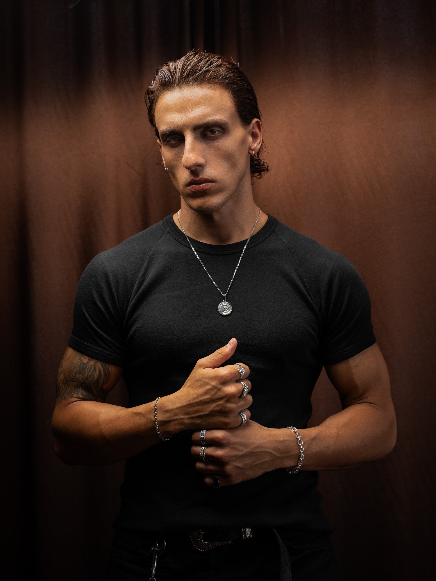 Man wearing a black t-shirt with visible jewelry against a brown background