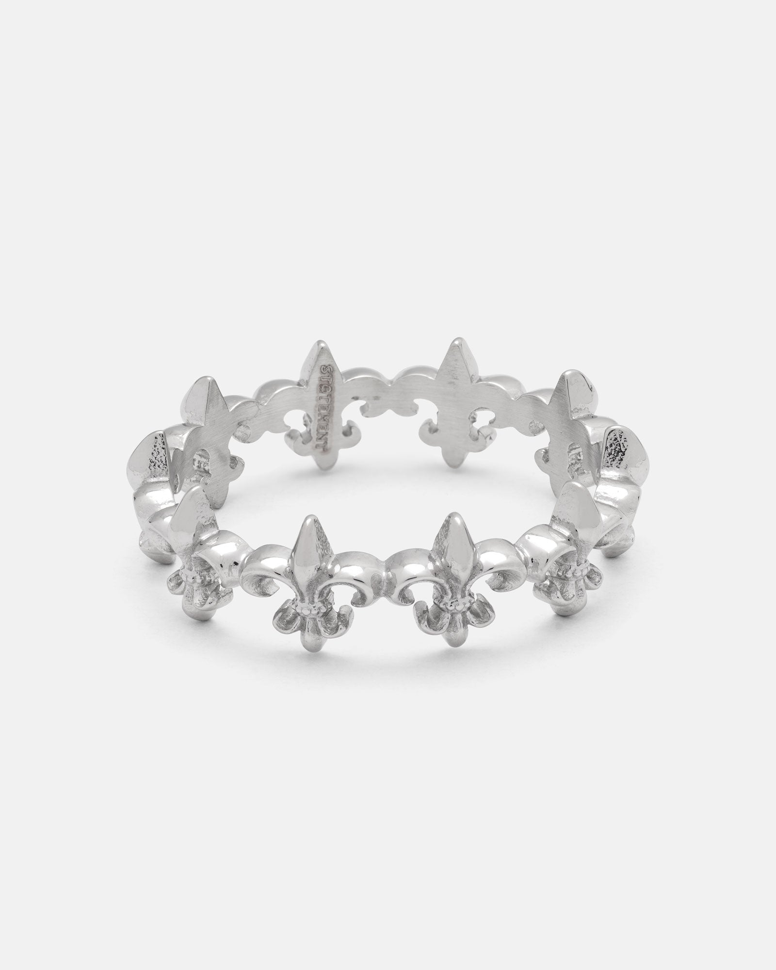 The “Fleur De Lis” Ring by Statement Collective is crafted in silver and features a repeating fleur-de-lis pattern around the band. Displayed on a white background, this stackable ring is perfect for creating a unique, layered look.