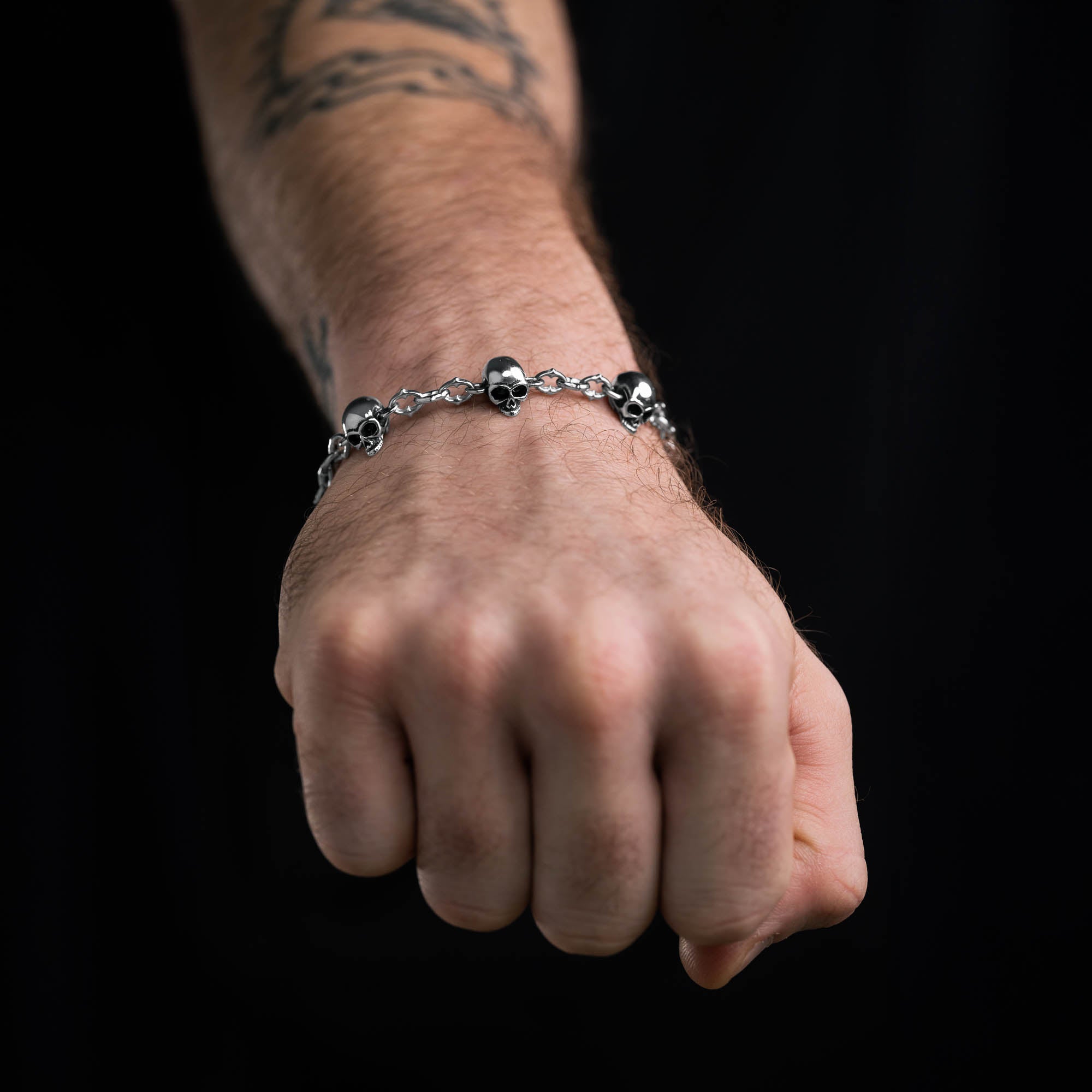 Silver spiked link bracelet with skull links all the way around, on male hand
