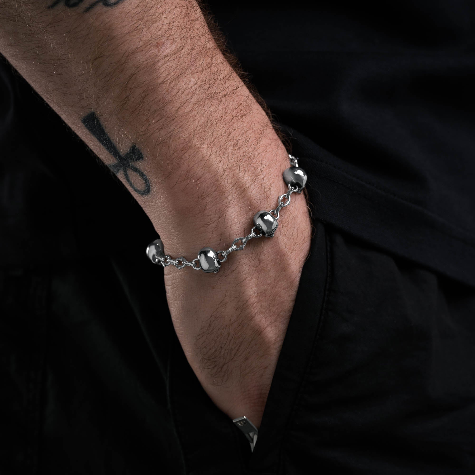 Silver spiked link bracelet with skull links all the way around, on male model