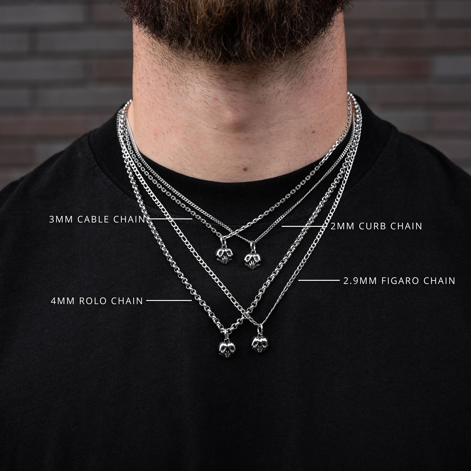 Man wearing multiple silver skull heart chain necklaces with labeled chain types against a brick wall background.