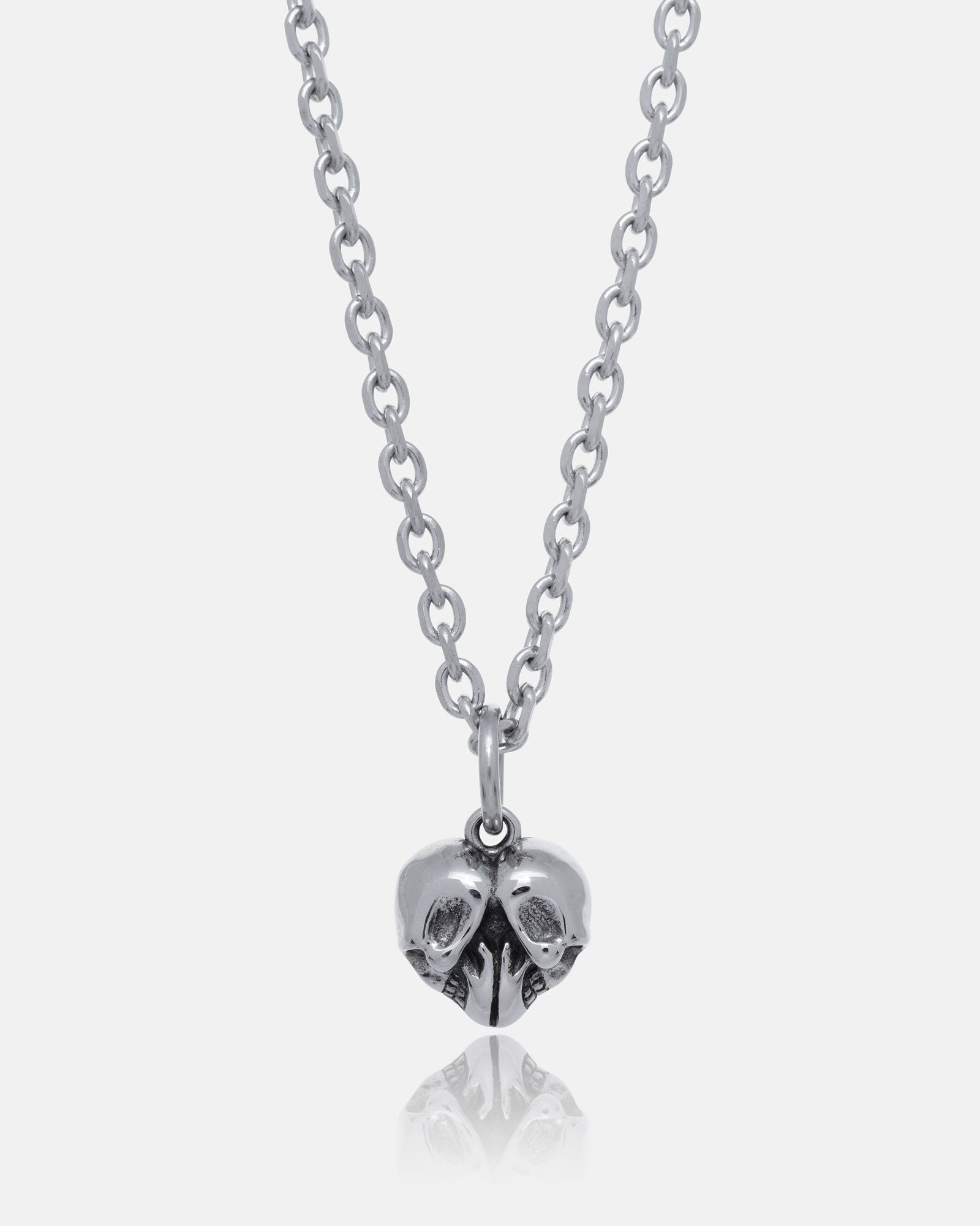 The Skull Heart Pendant is a stainless steel necklace featuring two small skulls joined at the side and facing opposite directions, showcasing dark romance jewelry against a plain white background.