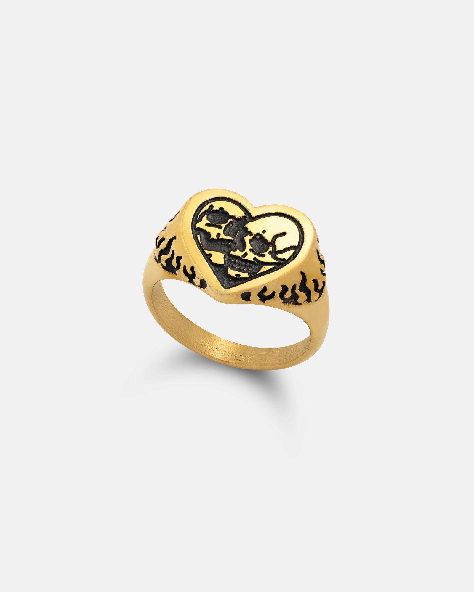 The Skull Heart Ring (Gold) is an 18k gold plated gothic ring with a black heart-shaped center featuring two skulls and bold black flame patterns along the band.