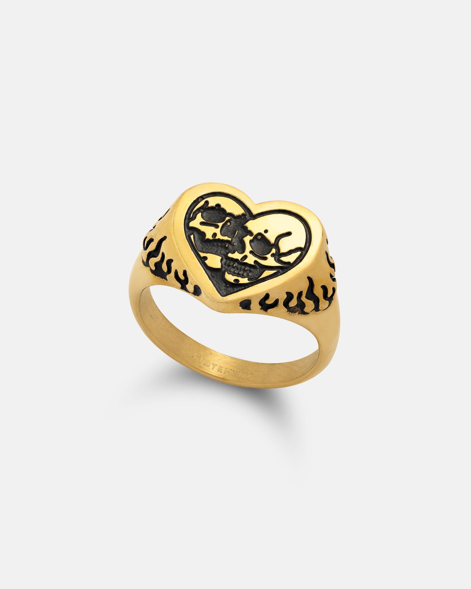 The Skull Heart Ring (Gold) is an 18k gold plated piece with a heart-shaped face, black skull and crossbones, bold black flame patterns on the band, and a plain white background—perfect for adding gothic flair.