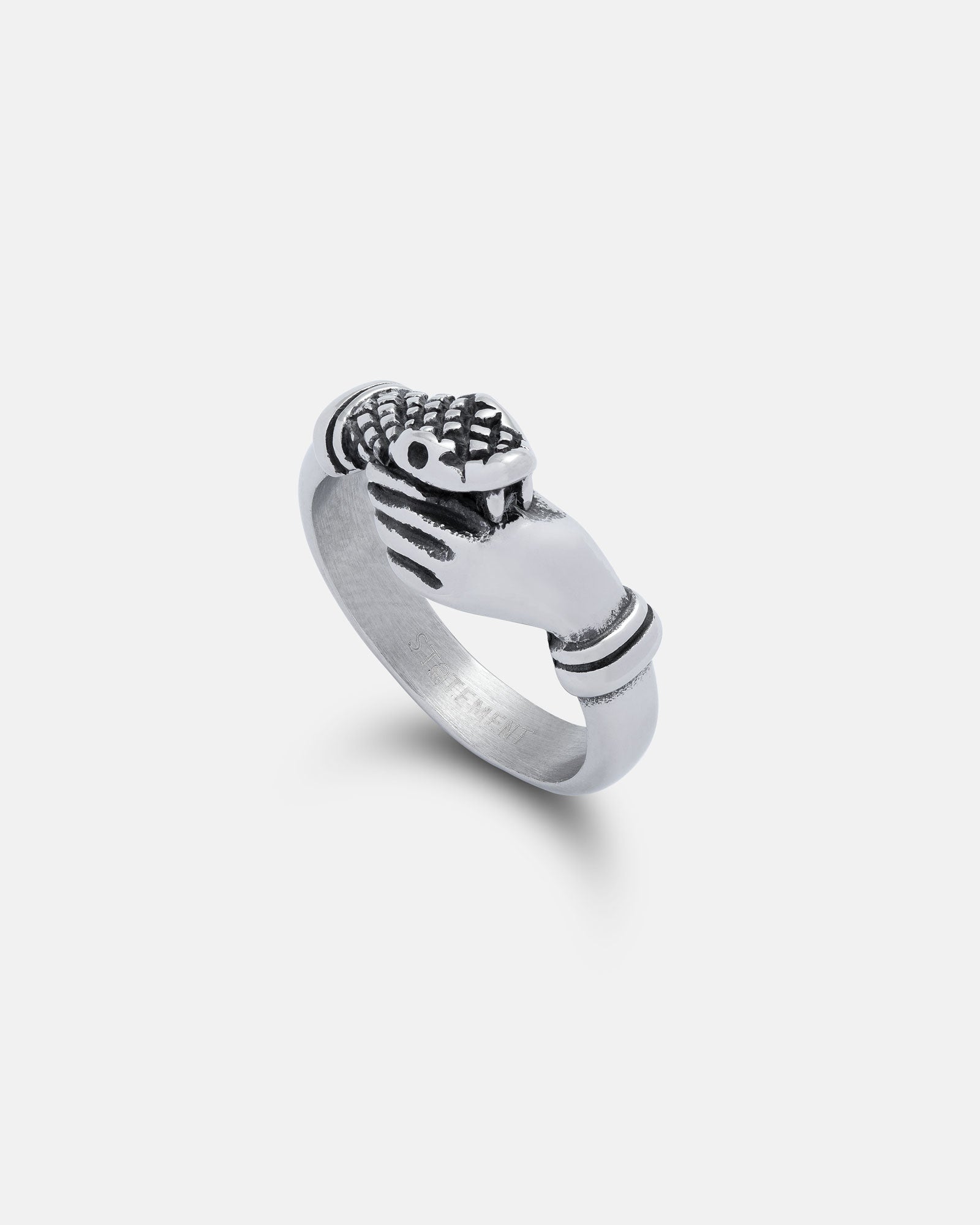 The Hand That Bites" Ring: a stainless steel piece with two hands holding a crowned heart in the classic Claddagh style, shown against a plain white background.