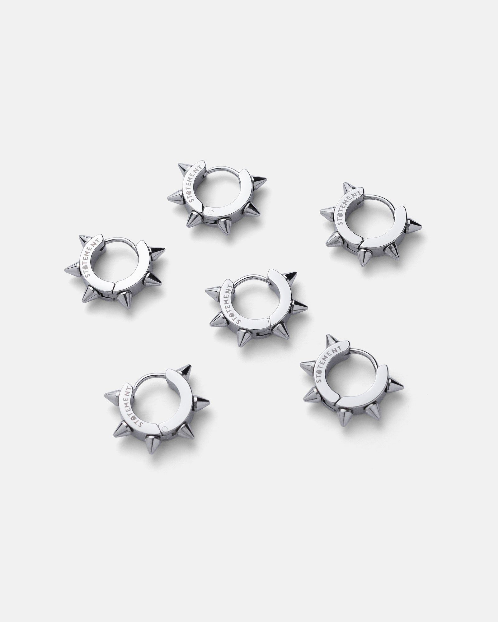 Six 8mm Spiked Hoop Earrings in a silver color are arranged in two rows on a plain light gray background. Each punk hoop earring features engraved text on the smooth stainless steel band section.