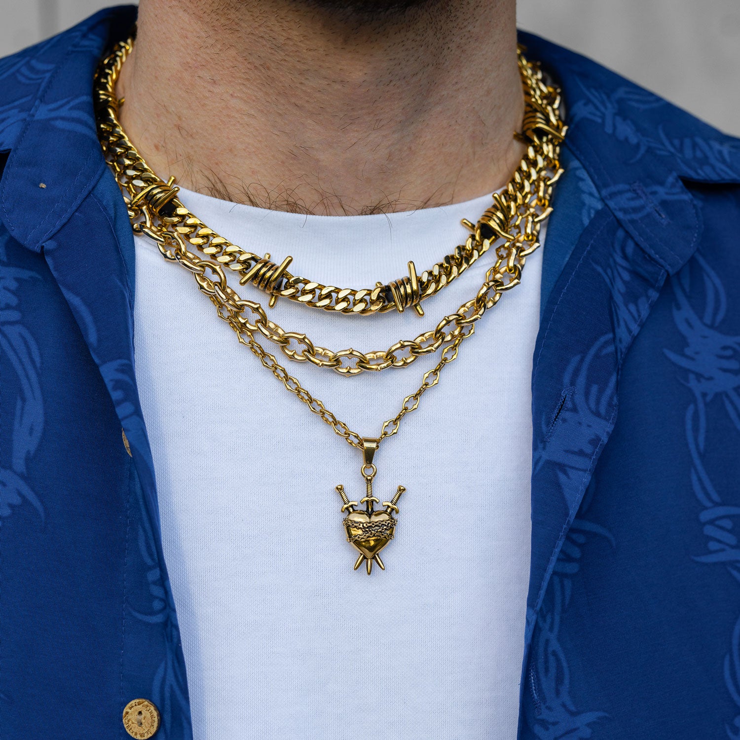 Gold chain set with barbed wire chain and spiked jewelry with cross pendant on mans body by Statement Collective