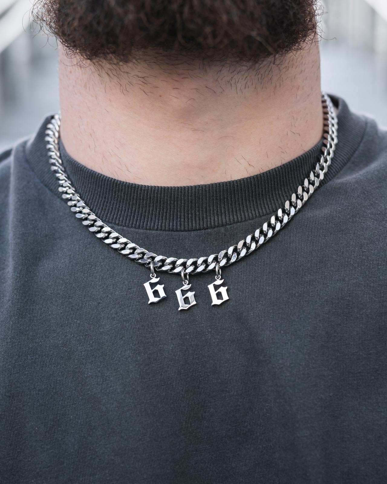 Wearing the Statement Piece Customisable Necklace by Statement Collective, featuring chunky Cuban links and number charms, over a dark grey crewneck, the focus is on the bold, personalised accessory adorning the neck and lower face.