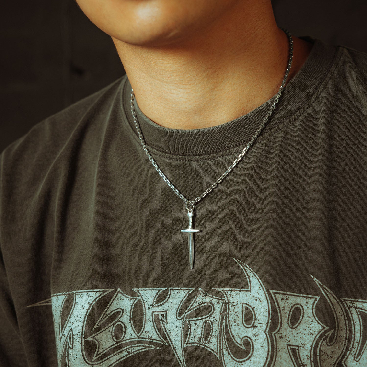 Silver chain with a dagger pendant on it, engraved with "Statement" on male model