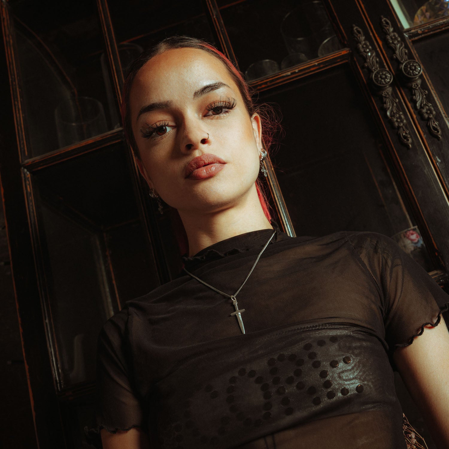 Silver chain with a dagger pendant on it, engraved with "Statement" on emale model with black mesh shirt and red hair