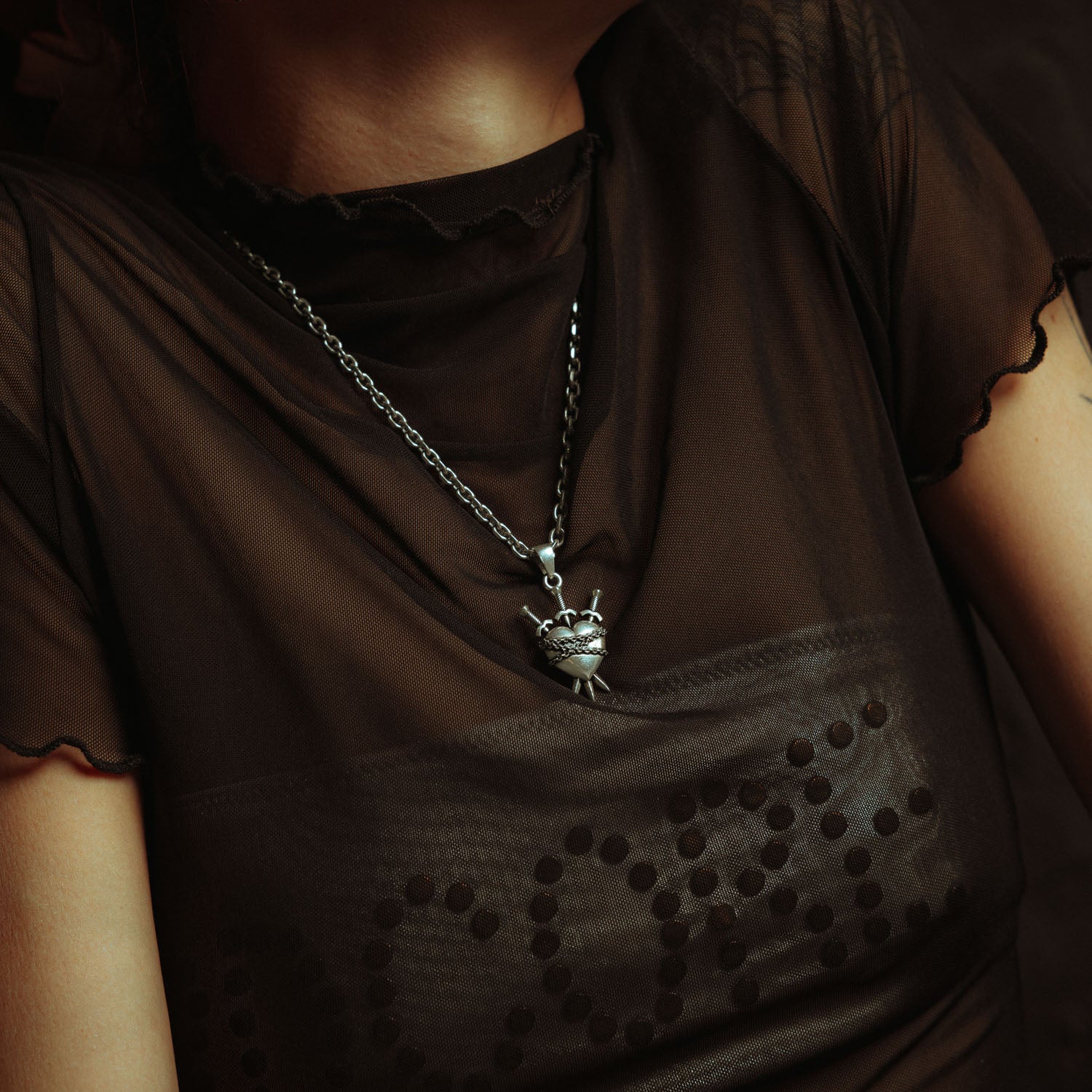 Silver heart pendant with 3 swords going through it and wrapped in chain on female model