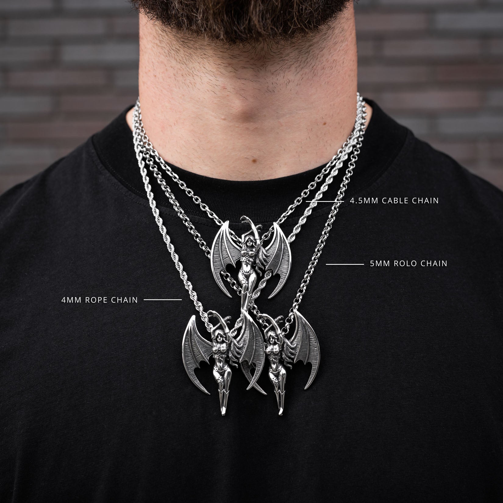 Silver necklace with detailed succubus pendant on a black shirt against a brick wall.