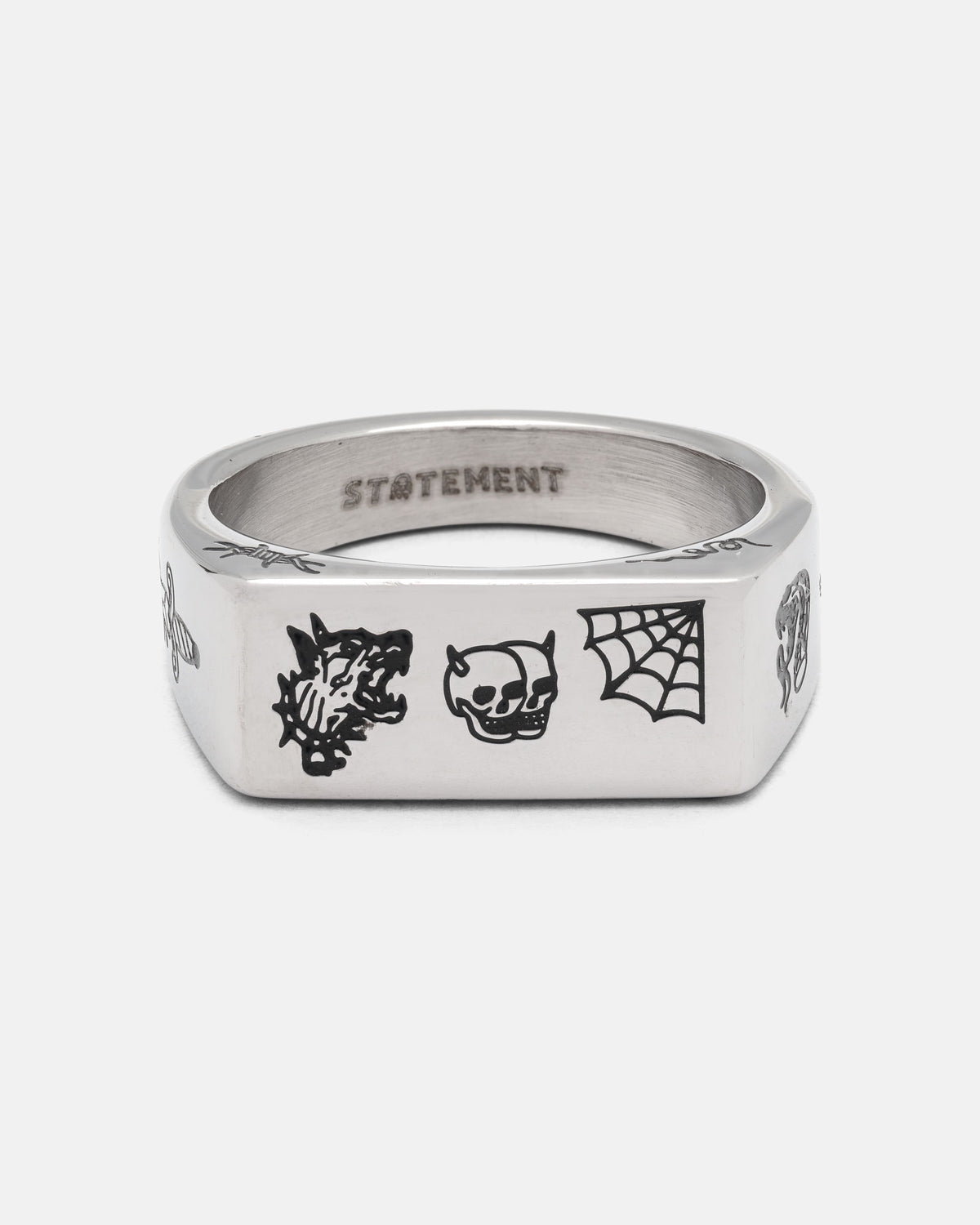Introducing the STATEMENT Tattoo Signet Ring: a bold stainless steel piece adorned with striking black engraved designs of a snarling wolf, skull, and spiderweb. The brand name “STATEMENT” is engraved on the inner surface of this standout ring.