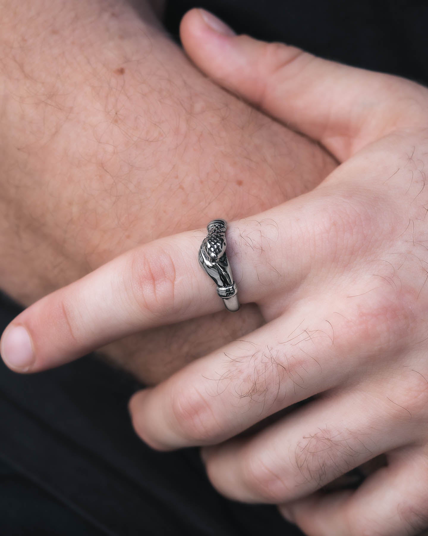 A close-up of a hand wearing "The Hand That Bites" Ring, shaped like a parrot perched on a branch, with the other hand gently touching the finger against a blurred background.