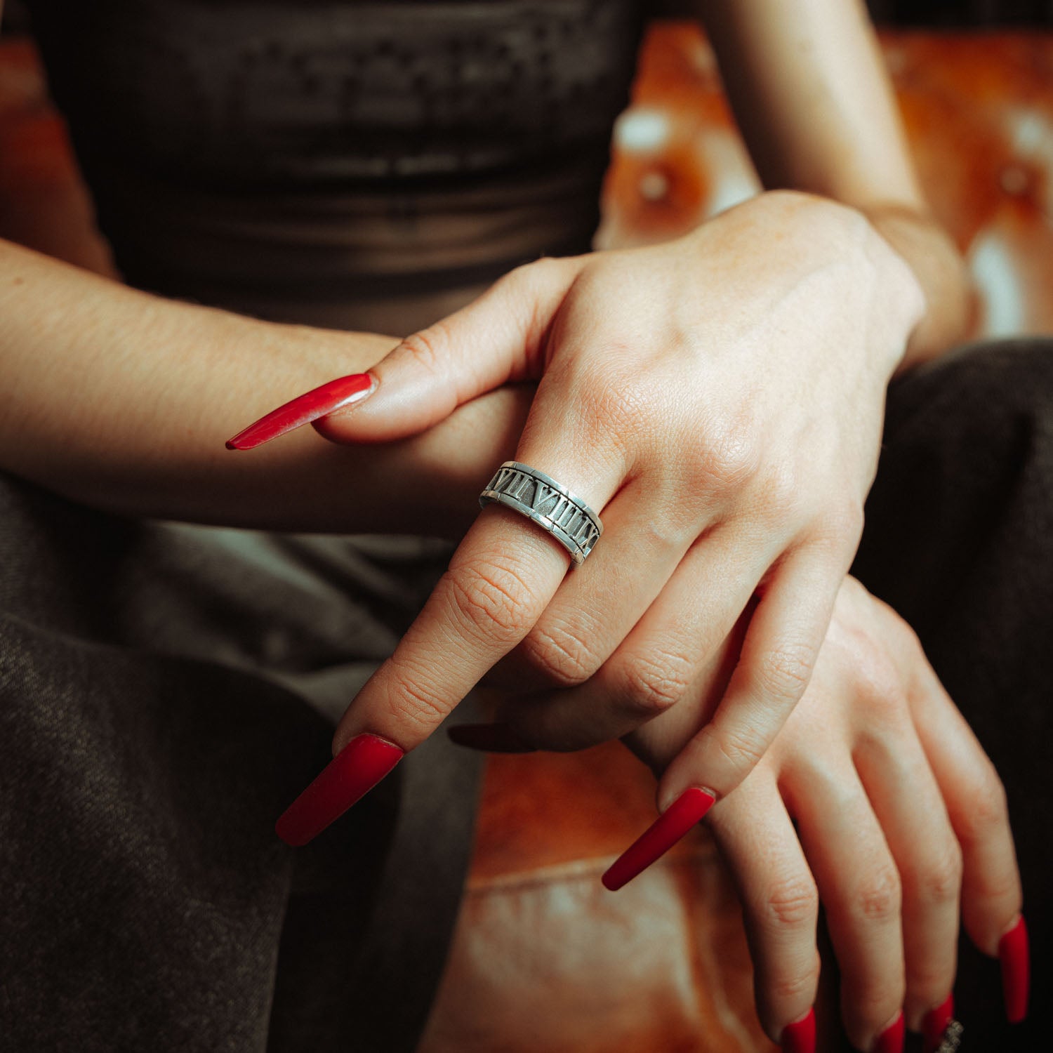 Sterling Silver band ring with roman numerals the entire way around it. on female hand with red nails