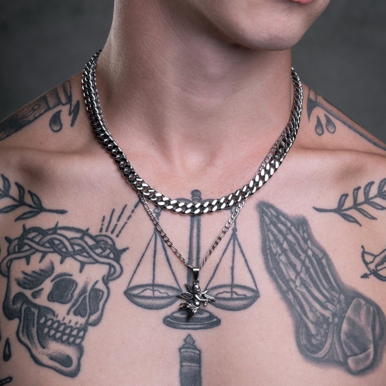 tattooed mans chest with silver cupid pendant necklace by statement collective